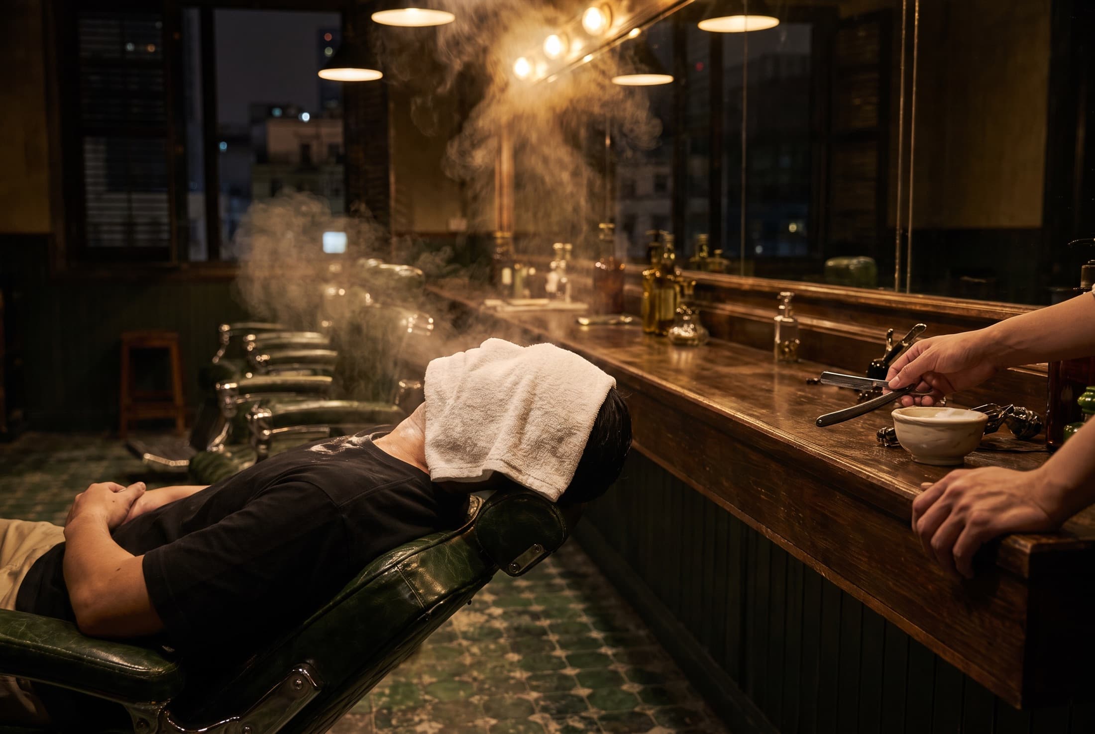 A client reclined flat with a steaming hot towel over his face, a straight razor and lather bowl on the counter